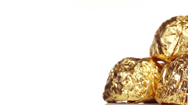 Chocolate bonbons wrapped in gold foil on a white background, Dolly shot
