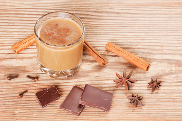 Glass of hot chocolate with cinnamon, cloves and star anise on rustic wooden table with space for text