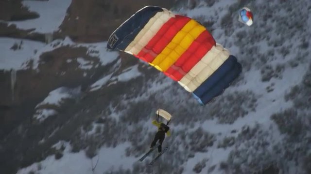 A base jumper descending then landing on snowy road. Shot in slow motion.