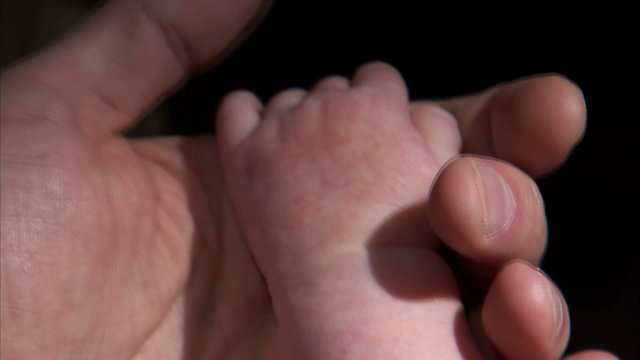 Close-up of a baby grasping an adult's hand.
