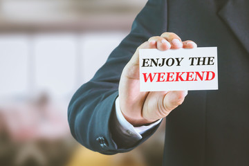 Businessman holding a white sign with the message enjoy the weekend. Can bring to the medium of...