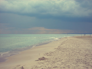 Long exotic white sandy beach on a cloudy day with dramatic sky. Beautifu beach landscape. Image filtered in faded, retro, Instagram style.