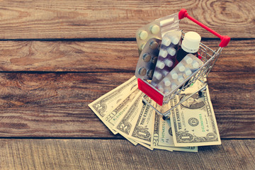 Shopping cart with pills, a syringe, candles, dollars on the old wood background. Toned image.