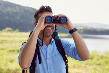 Handsome man looking through binoculars during hiking adventure