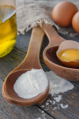 Wooden spoon with flour, eggs and a bottle of oil