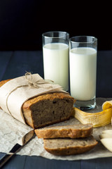 Banana bread with glasses of milk on baking paper