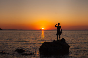A man standing on the shore watching the sunset
