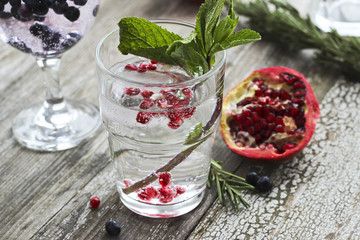 Glasses of water with ice, rosemary, mint, pomegranate and blueberry