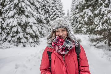 Fototapeta na wymiar Woman winter hiking. Beautiful young woman enjoying the falling snow dressed in a winter scarf and cap and with a satchel on her back with copyspace.