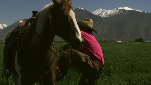 Slow handheld shot of a cowboy getting on his horse