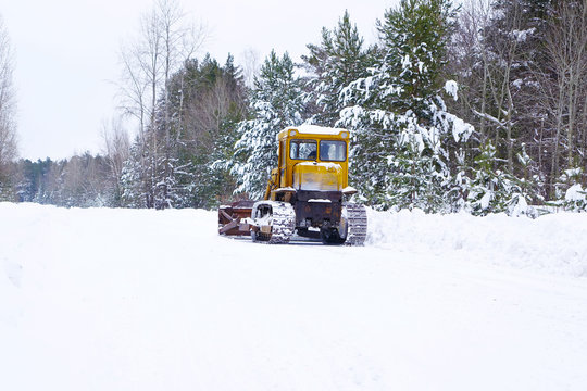 Crawler Tractor grader cleans snow on a forest road. Winter background. Medium shot.