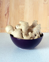 Ginger roots in dark bowl on on kitchen table. Vertical view closeup