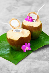 Fototapeta na wymiar Drink Coconut Water. Tropical Cocktail With Refreshing Detox Organic Raw Coconut Milk, With Drinking Straw And Orchid Flower. Diet. Nutrition And Hydratation. Vitamins. Healthy Lifestyle.