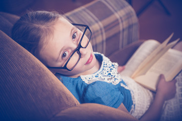 Girl reading a book at home sitting in an armchair.