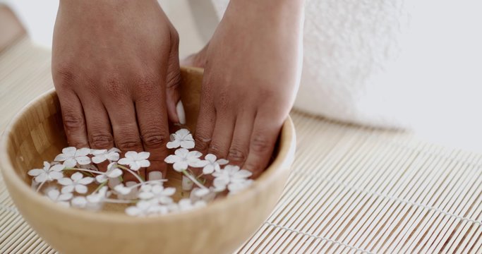 Hands with manicure relaxing in bowl of water with flowers petals