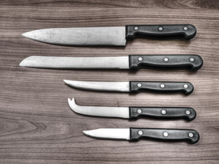 Set of kitchen knives on wood work surface. Filtered image for retro effect.