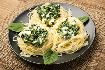 Italian pasta with spinach and feta on black plate on the wooden background.