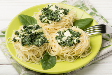 Italian pasta with spinach and feta on green plate on the wooden background.