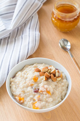 Oatmeal porridge with dried apricots and chopped almonds on bright wooden table. Jar of honey on background. Selective focus. Bright healthy breakfast image
