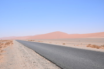 Fototapeta na wymiar Straße in der Wüste mit Dünen im Hintergrund