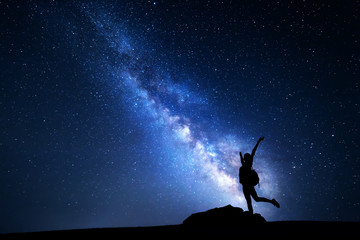Milky Way. Night sky with stars and silhouette of a happy woman with backpack and raised up arms....