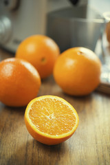 Close up shot of half sliced fresh orange on wooden kitchen table in front of juicer machine.