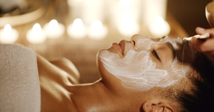 Cosmetologist smears cosmetic mask on the face of the woman in the spa salon