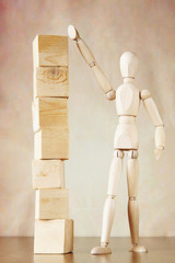Man builds high pile of cubes. Conceptual image with wooden puppet