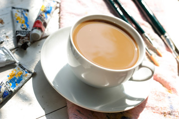 a cup of milkcoffee between brushes and ink tubes