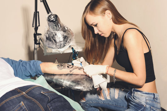 Young beautiful woman tattooer showing process of making a tattoo black skull with crown design.