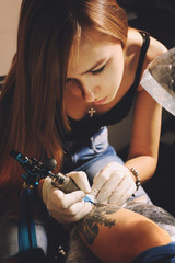 Woman tattoo master in a process of creation tattoo with a crown on a man`s hand.