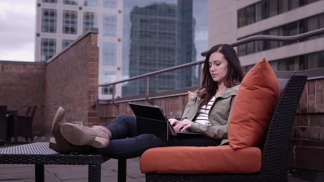 View of woman relaxing on roof top typing on laptop.