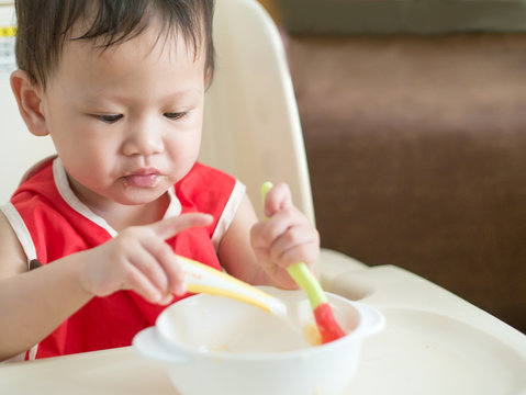 Asian toddler learn to eat meal herself.