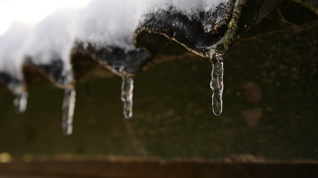 Water running over roof increasing icicles hanging down with water drops