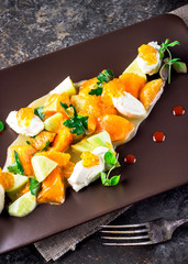 Salad with goat cheese and tangerines on brown plate.