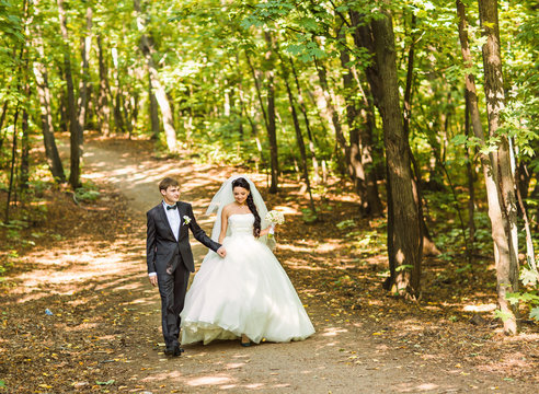 Bride and Groom at wedding Day walking Outdoors. Newlyweds in the park.