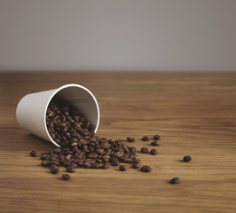 Blank paper cup with roasted coffee beans on wooden table