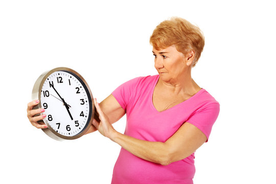 Worried senior woman holding big clock