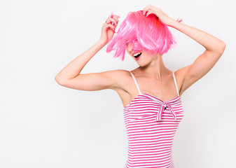 Cheerful young woman in pink wig and dancing on white background