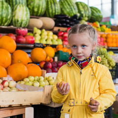 Fototapeta na wymiar Девочка на рынке выбирает фрукты