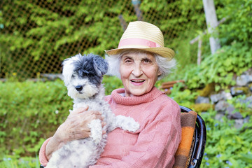 beautiful Senior smiling woman with straw hat hugging her small white poodle dog in the mountain