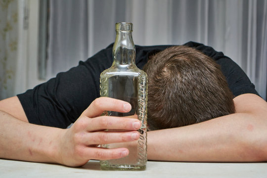 Drunk guy holding a bottle of vodka lying on the table close-up.