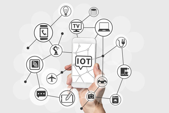 Internet of Things (IOT) concept with hand holding modern white and silver smart phone. Connected devices in the cloud as technology background
