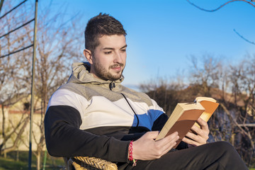 young handsome man sitting on chair in a garden  reading a book