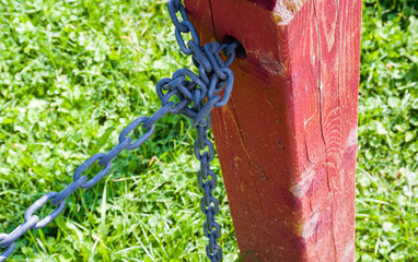 Red fence post with tied metal chain against grass