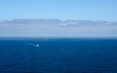 Three boats in distance on blue ocean under forming clouds