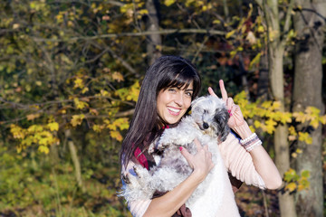 beautiful smiling young woman hugging her small white poodle dog in the autumn park
