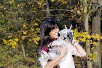 Naklejka na ściany i meble beautiful smiling young woman hugging her small white poodle dog in the autumn park