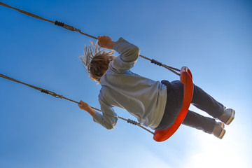 Boy swinging very high, blue sky in background - obrazy, fototapety, plakaty
