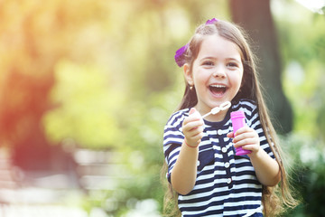 Naklejka premium Happy little girl with bubbles in the park